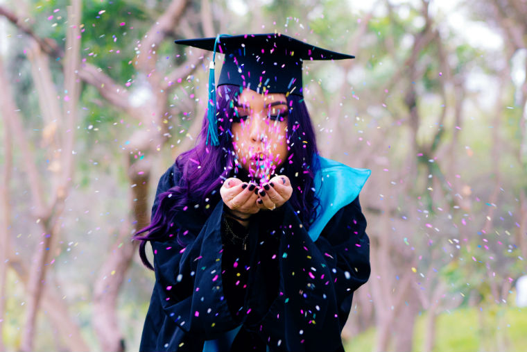A graduate in cap and gown blowing glitter